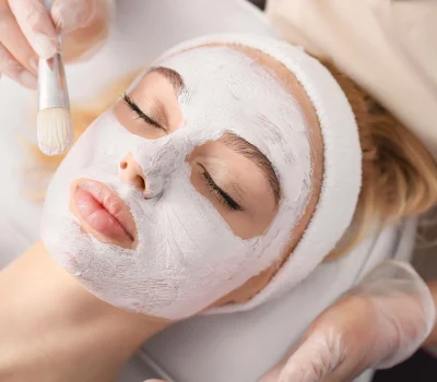 Cosmetologist applying mask onto face of woman in beauty salon